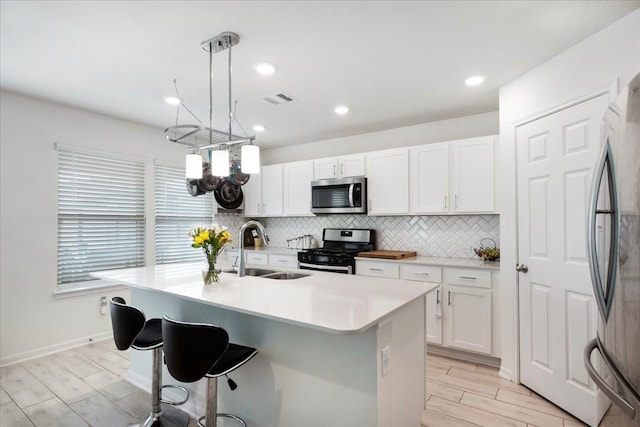 kitchen featuring white cabinetry, sink, appliances with stainless steel finishes, decorative light fixtures, and an island with sink