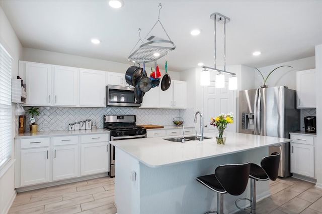 kitchen with white cabinetry, appliances with stainless steel finishes, decorative light fixtures, sink, and an island with sink