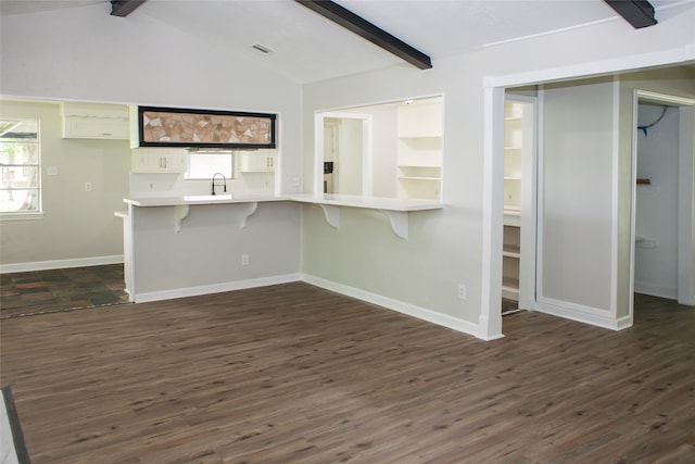 kitchen featuring kitchen peninsula, a wealth of natural light, a breakfast bar area, vaulted ceiling with beams, and dark wood-type flooring