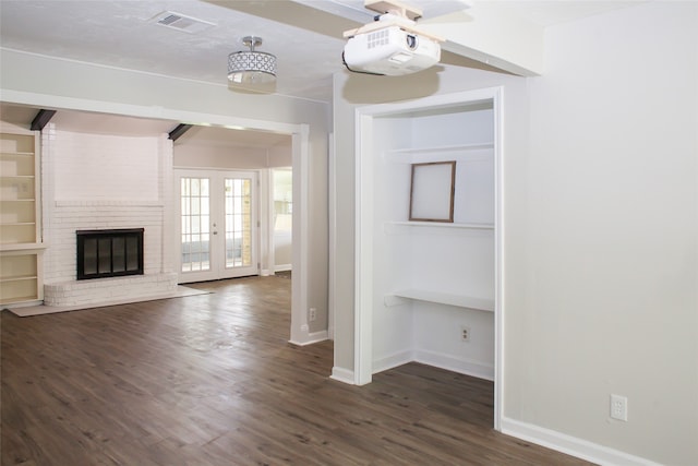 unfurnished living room with brick wall, a brick fireplace, dark hardwood / wood-style flooring, and french doors