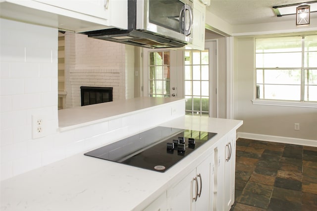 kitchen with black electric stovetop, a fireplace, a textured ceiling, white cabinets, and dark tile floors