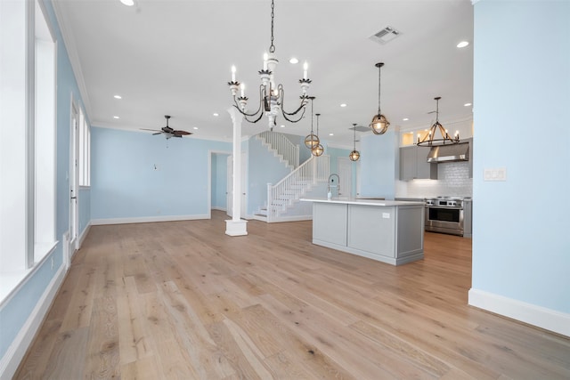 kitchen with light hardwood / wood-style floors, hanging light fixtures, a center island with sink, and stainless steel range oven