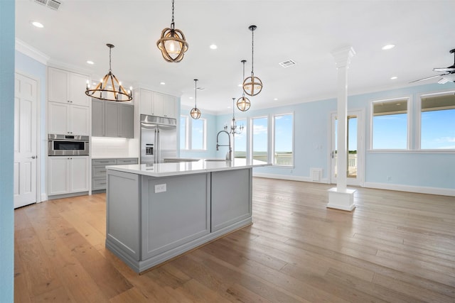 kitchen with light countertops, appliances with stainless steel finishes, light wood-style floors, a sink, and an island with sink