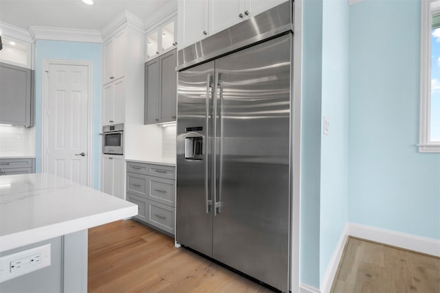 kitchen with appliances with stainless steel finishes, glass insert cabinets, light wood-style flooring, and tasteful backsplash