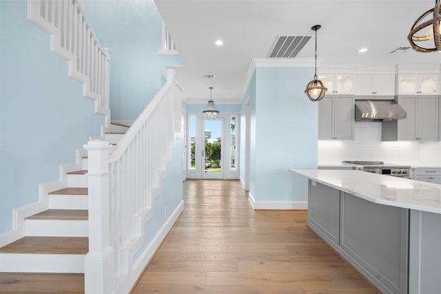 kitchen with visible vents, light stone counters, crown molding, light wood-type flooring, and wall chimney range hood