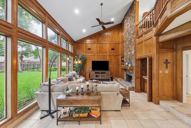 living room with a fireplace, ceiling fan, high vaulted ceiling, wooden walls, and light tile floors