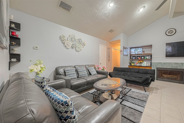 tiled living room with high vaulted ceiling, a tiled fireplace, ceiling fan, and a textured ceiling