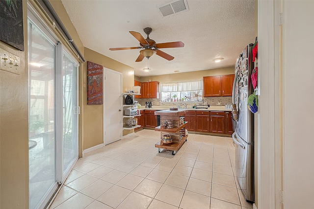 kitchen with a textured ceiling, backsplash, stainless steel refrigerator, ceiling fan, and light tile floors