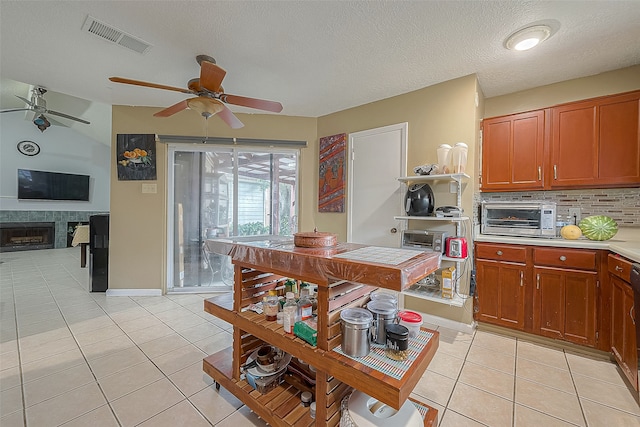 kitchen featuring a textured ceiling, a tiled fireplace, ceiling fan, and light tile flooring