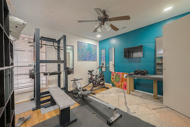 workout room with a textured ceiling, wood-type flooring, and ceiling fan