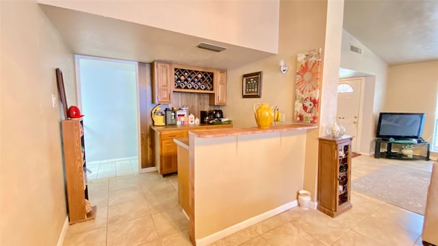 kitchen featuring kitchen peninsula, a breakfast bar, light tile floors, and lofted ceiling