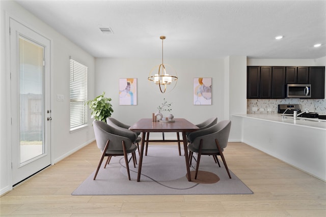 dining room featuring sink, light wood-type flooring, and an inviting chandelier