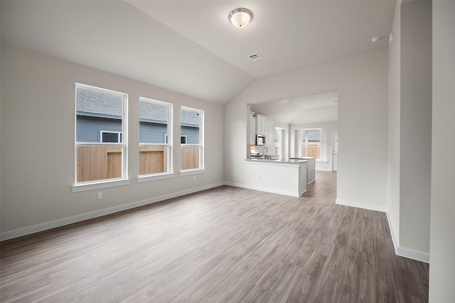 unfurnished living room with lofted ceiling, sink, and light hardwood / wood-style flooring