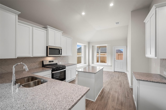 kitchen with appliances with stainless steel finishes, white cabinetry, a kitchen island, and sink