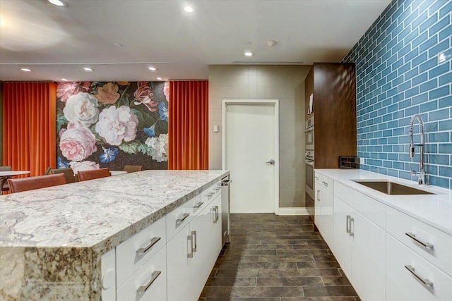 kitchen featuring oven, a kitchen island, white cabinetry, and sink