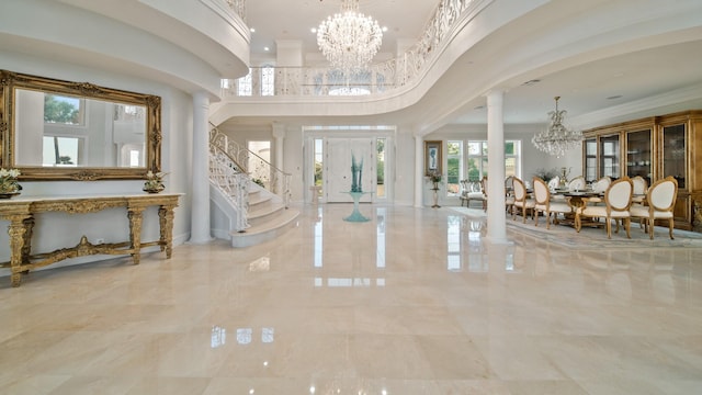 foyer featuring crown molding, a towering ceiling, a chandelier, and decorative columns