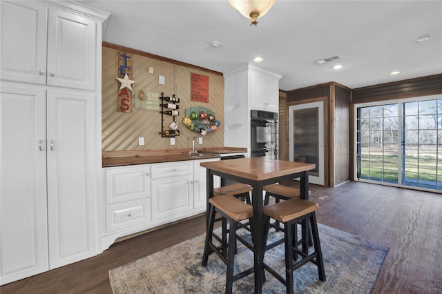 dining space featuring dark hardwood / wood-style floors, ornamental molding, wood walls, and sink