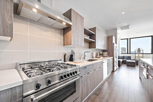 kitchen with decorative backsplash, wall chimney exhaust hood, stainless steel appliances, sink, and dark hardwood / wood-style flooring