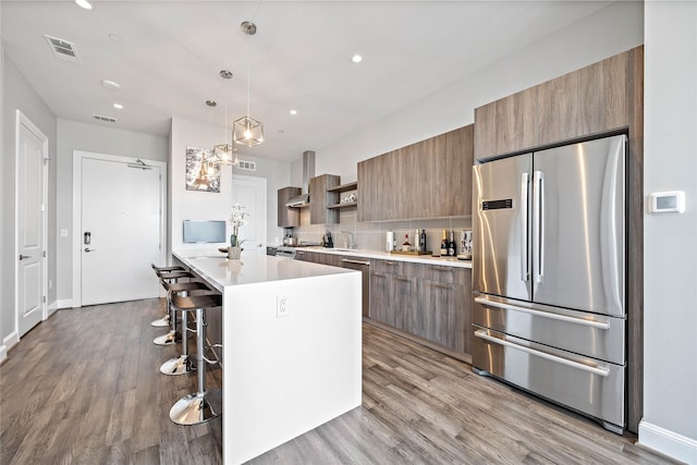 kitchen featuring appliances with stainless steel finishes, hanging light fixtures, light hardwood / wood-style floors, wall chimney exhaust hood, and a breakfast bar area