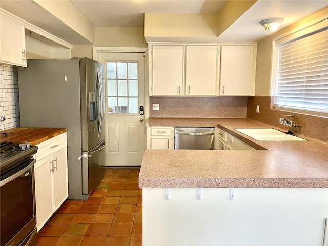 kitchen with backsplash, tile floors, sink, white cabinetry, and appliances with stainless steel finishes