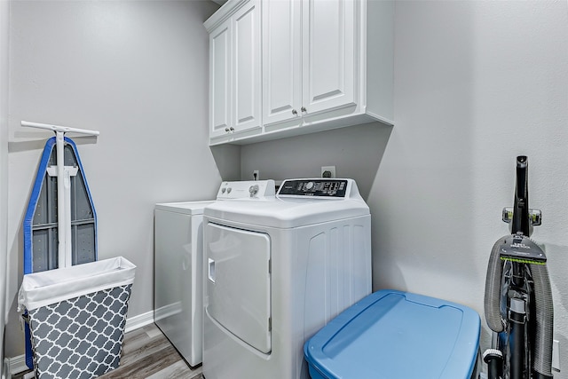 laundry room with washing machine and clothes dryer, hardwood / wood-style flooring, and cabinets