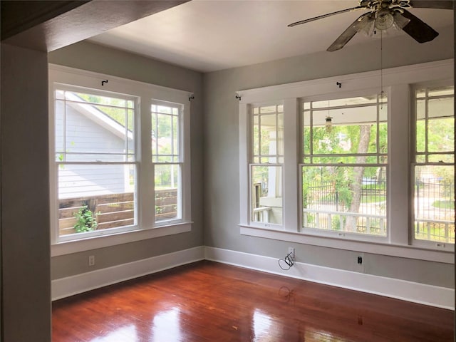 unfurnished room featuring a wealth of natural light, dark wood finished floors, baseboards, and ceiling fan