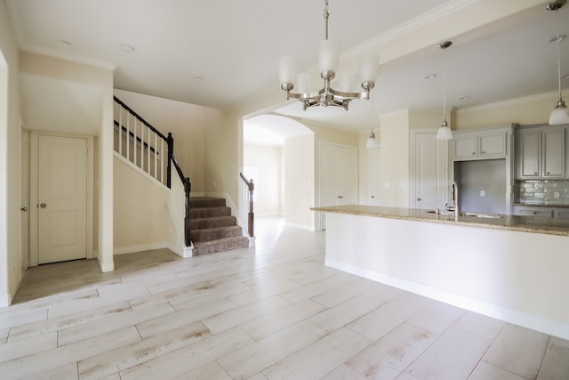 kitchen with hanging light fixtures, an inviting chandelier, light stone counters, backsplash, and sink