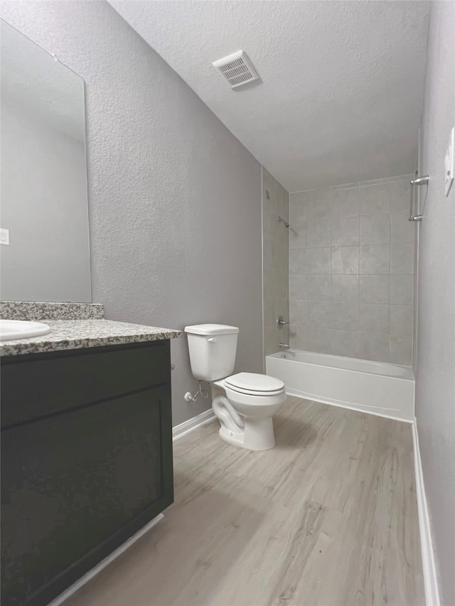 full bathroom featuring hardwood / wood-style floors, tiled shower / bath, a textured ceiling, toilet, and vanity