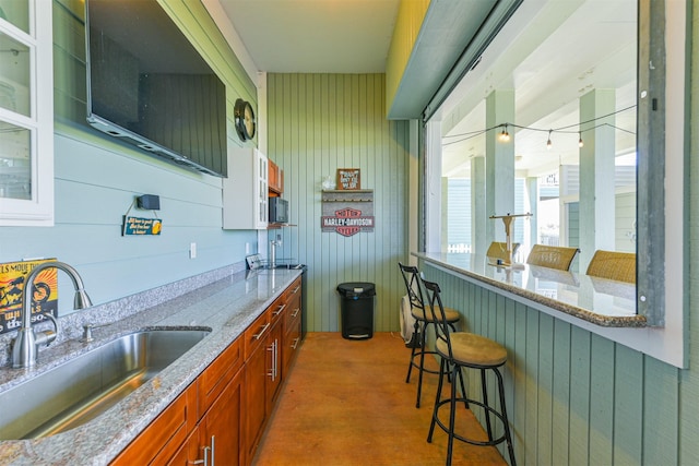 bar with sink, wood walls, and light stone counters