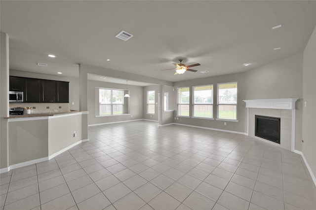 unfurnished living room featuring plenty of natural light, light tile flooring, a tile fireplace, and ceiling fan