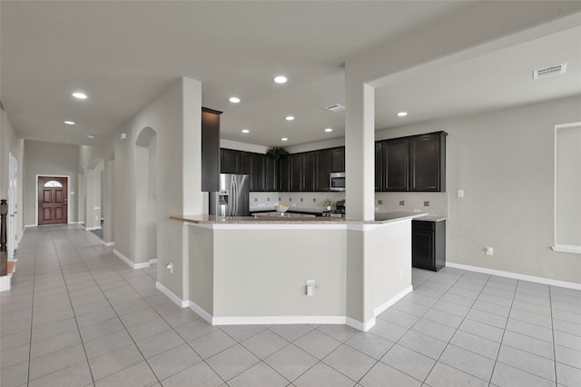 kitchen featuring appliances with stainless steel finishes, kitchen peninsula, dark brown cabinetry, tasteful backsplash, and light tile floors