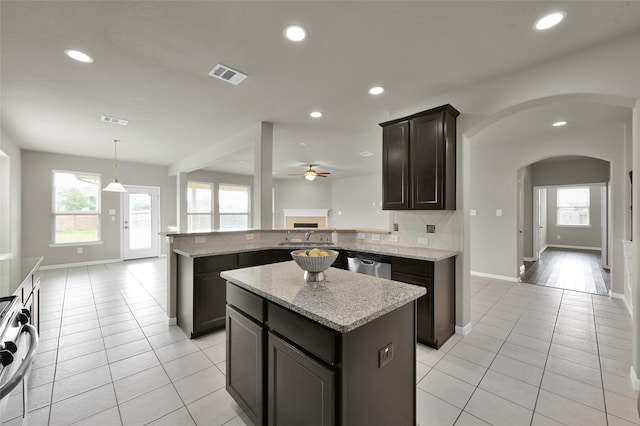 kitchen with decorative light fixtures, light tile flooring, kitchen peninsula, backsplash, and light stone countertops