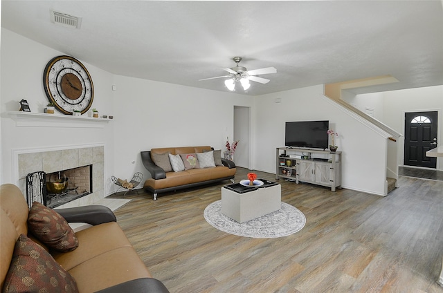 living area featuring ceiling fan, visible vents, a tiled fireplace, wood finished floors, and stairs