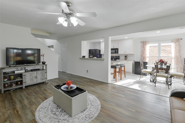 living area with baseboards, a ceiling fan, and wood finished floors