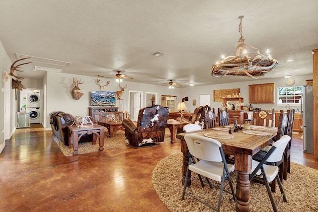 dining area with stacked washer and dryer, ceiling fan with notable chandelier, concrete flooring, and a textured ceiling