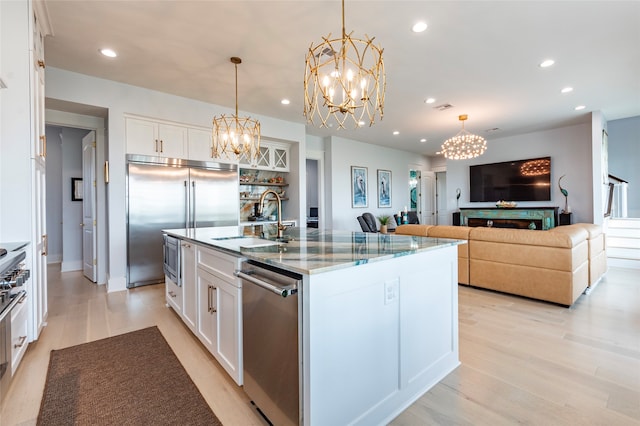 kitchen featuring stainless steel appliances, white cabinets, sink, an island with sink, and pendant lighting