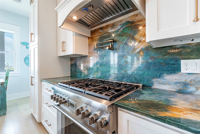 kitchen featuring high end range, white cabinets, backsplash, and premium range hood