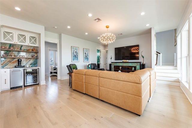 living room with light wood finished floors, beverage cooler, visible vents, stairway, and a bar