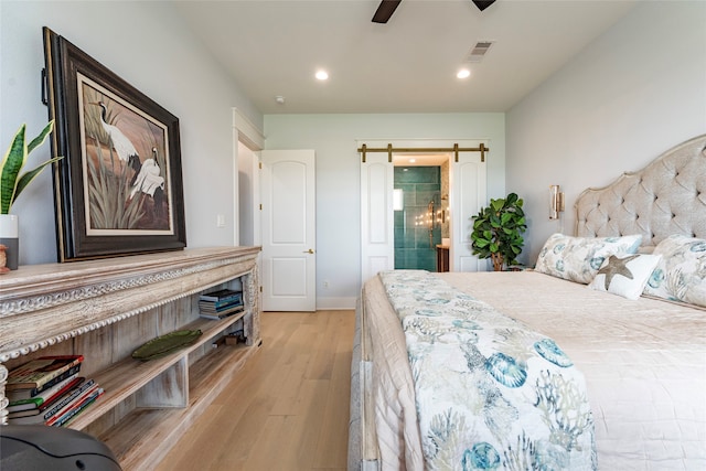 bedroom featuring a barn door, ceiling fan, and light hardwood / wood-style flooring