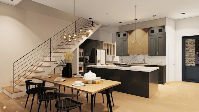 kitchen with pendant lighting, sink, light stone countertops, an island with sink, and light wood-type flooring