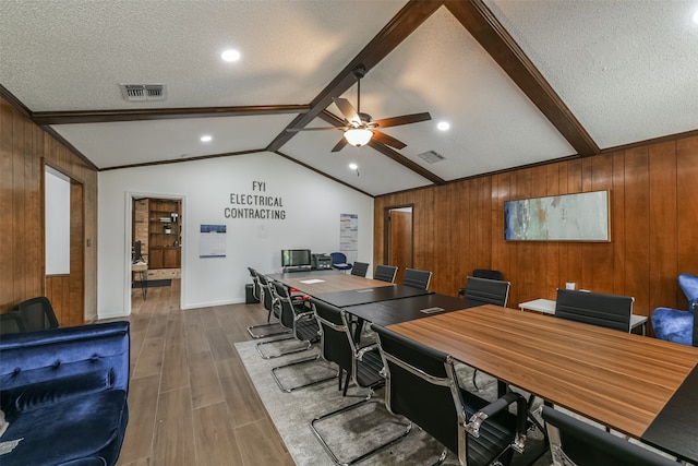 dining space with ceiling fan, vaulted ceiling with beams, a textured ceiling, wood walls, and hardwood / wood-style flooring