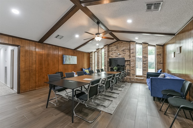 dining space featuring wood walls, ceiling fan, vaulted ceiling with beams, wood-type flooring, and a textured ceiling