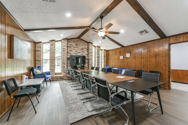 dining space featuring wooden walls, ceiling fan, lofted ceiling with beams, and a textured ceiling