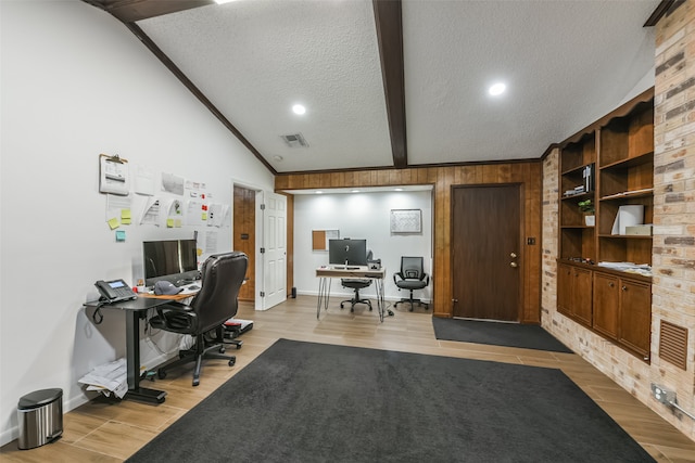 office area with light wood-type flooring, a textured ceiling, brick wall, and vaulted ceiling with beams