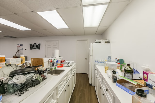 kitchen with a paneled ceiling, dark hardwood / wood-style flooring, white cabinets, sink, and white fridge