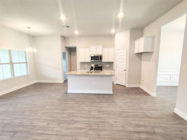 kitchen with white cabinetry, a kitchen island with sink, stainless steel appliances, light stone counters, and light wood-type flooring