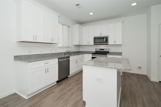 kitchen featuring appliances with stainless steel finishes, light stone counters, sink, a center island, and white cabinetry