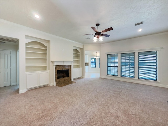 unfurnished living room with built in shelves, ceiling fan, a high end fireplace, crown molding, and light carpet