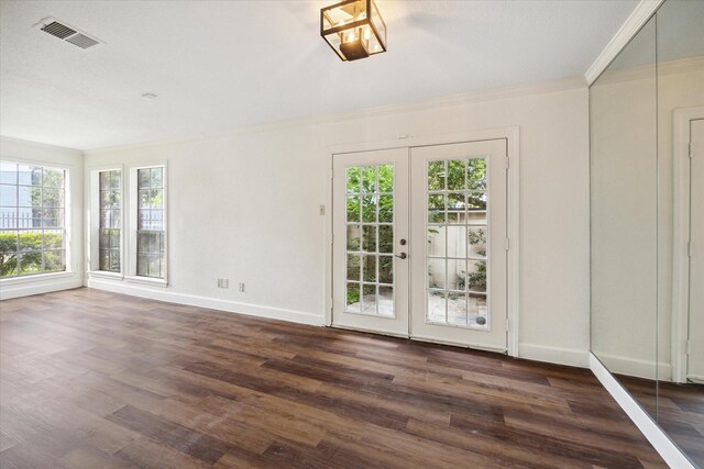 empty room with plenty of natural light, dark hardwood / wood-style flooring, ornamental molding, and french doors