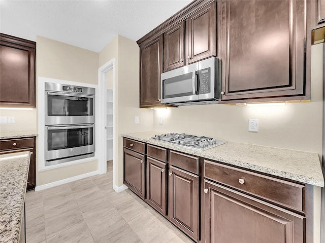 kitchen with appliances with stainless steel finishes, light stone counters, and dark brown cabinets